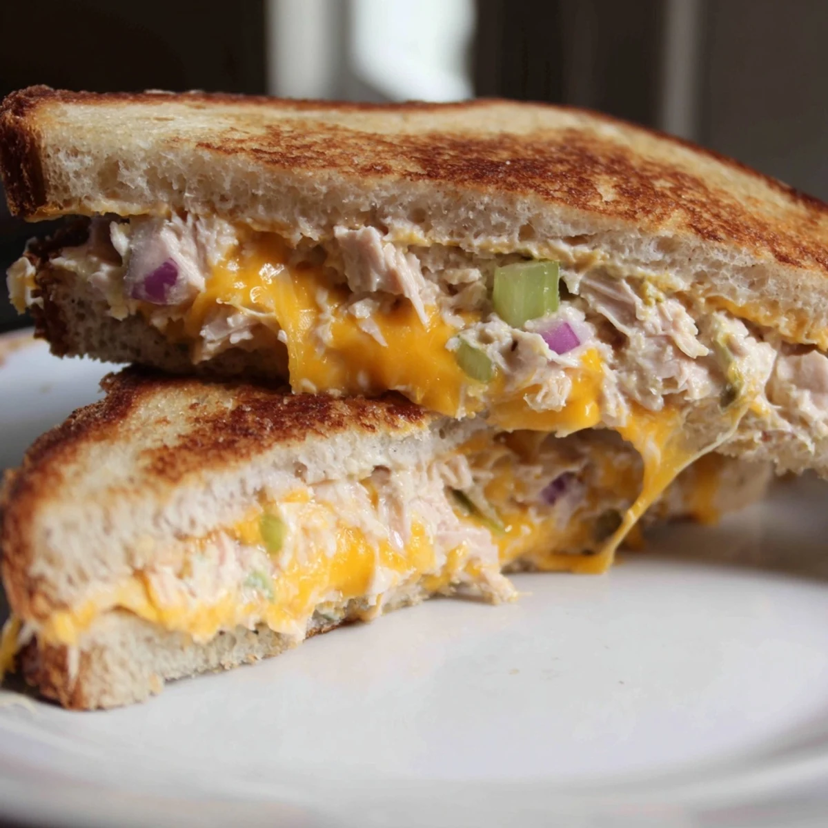 Close-up view of a spicy tuna melt, highlighting the toasted bread, melted cheese, and vibrant red tomato slices.