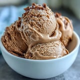 Hojicha ice cream is scooped into a bowl with toasted sesame seeds, showing its creamy texture.