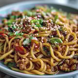 Korean Turkey Fried Noodles served in a white bowl with colorful vegetables and toasted sesame seeds.