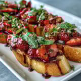 Fresh strawberry bruschetta with balsamic and mint served on golden toasted baguette slices, perfect for summer gatherings.
