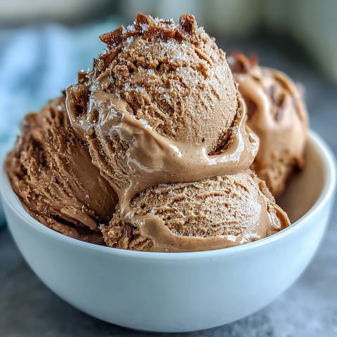 Hojicha ice cream is scooped into a bowl with toasted sesame seeds, showing its creamy texture.