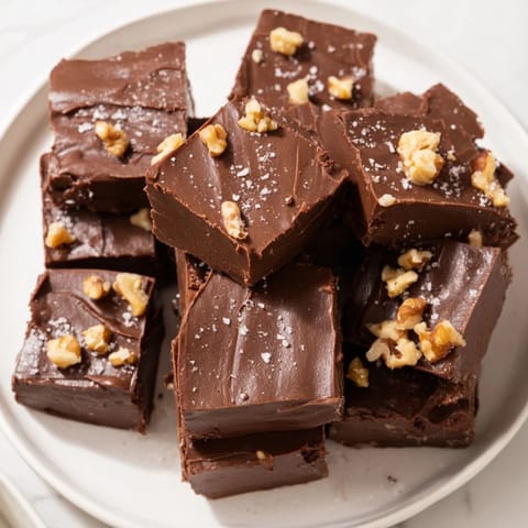 Homemade easy chocolate fudge, glistening, with optional chopped nuts and vanilla aroma.