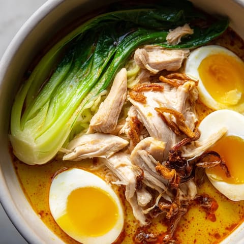 A vibrant Thai Miso Ramen Bowl features tender chicken, soft-boiled eggs, and fresh bok choy in a rich, aromatic broth.
