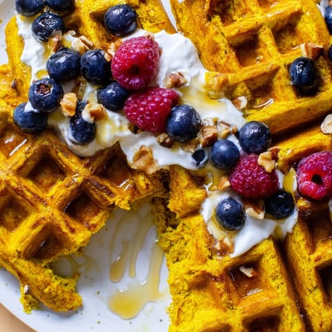 A close-up view of golden Anti-Inflammatory Adaptogenic Turmeric Waffles topped with creamy yogurt and sliced banana.
