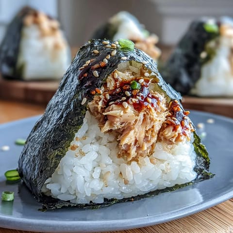 A handheld Japanese rice ball with spicy tuna filling, wrapped in nori for a savory sushi-inspired snack.  